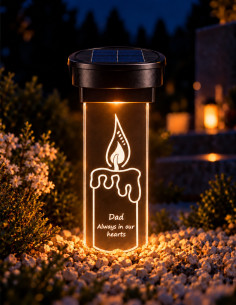 Solar grave candle with engraved flame and English dedication, glowing in a cemetery at night