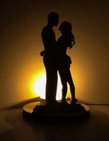 Silhouette romantique d’un couple enlacé éclairée par une bougie LED